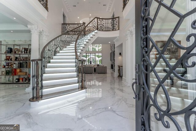 foyer with ornate columns, ornamental molding, and a towering ceiling