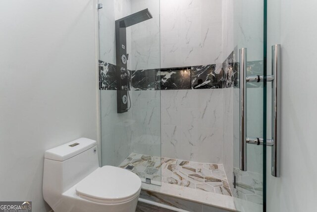 bathroom featuring a shower with door and toilet