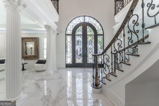 foyer entrance with a high ceiling, decorative columns, french doors, and ornamental molding