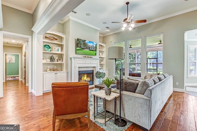 living room featuring light wood-type flooring, crown molding, ceiling fan, and a fireplace