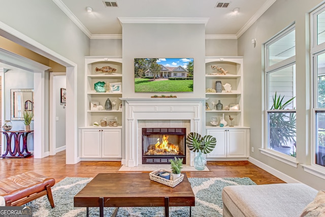 living room featuring built in features, light hardwood / wood-style floors, crown molding, and a tiled fireplace