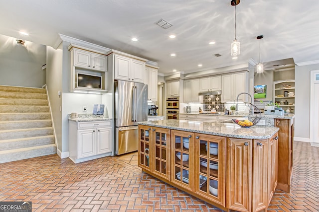 kitchen featuring a kitchen island, light stone counters, crown molding, appliances with stainless steel finishes, and decorative light fixtures