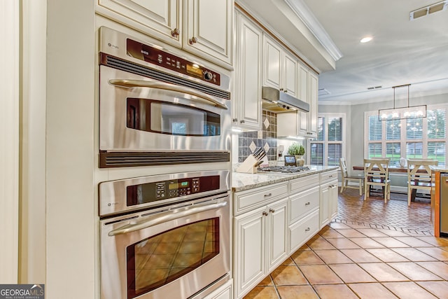 kitchen with light stone countertops, stainless steel appliances, crown molding, an inviting chandelier, and light tile patterned floors