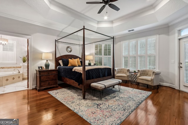 bedroom featuring ceiling fan, connected bathroom, dark wood-type flooring, a tray ceiling, and crown molding