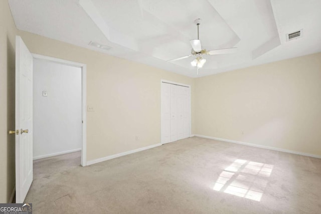 empty room with a tray ceiling, light colored carpet, and ceiling fan