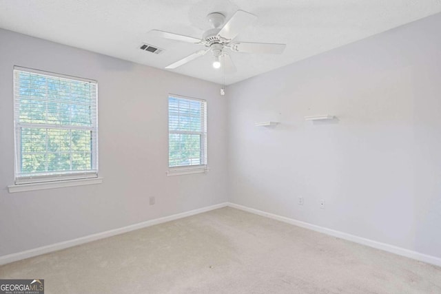 empty room featuring light colored carpet, a wealth of natural light, and ceiling fan