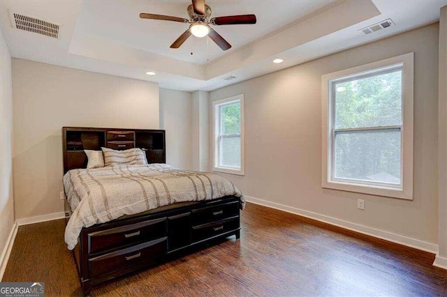 bedroom with dark wood-style floors, visible vents, a raised ceiling, and baseboards
