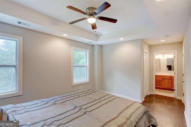 bedroom featuring ceiling fan, multiple windows, ensuite bath, and hardwood / wood-style floors