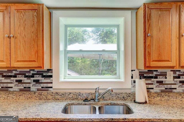 kitchen featuring tasteful backsplash, light stone counters, and a sink
