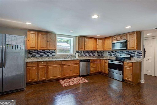 kitchen featuring brown cabinetry, stainless steel appliances, backsplash, a sink, and dark wood-type flooring