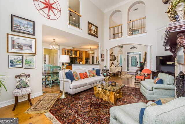 living room with a towering ceiling, ornate columns, ornamental molding, hardwood / wood-style flooring, and an inviting chandelier