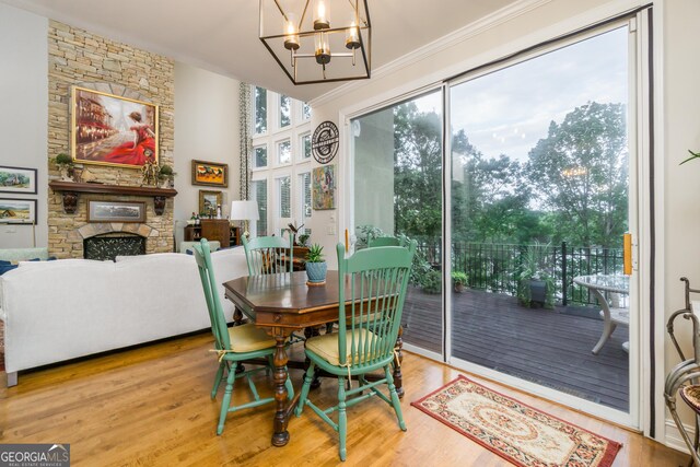 dining space with wood-type flooring, an inviting chandelier, a stone fireplace, and ornamental molding