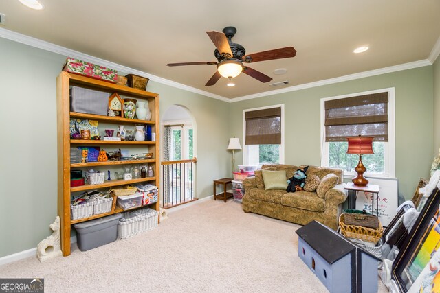 living area with carpet, ceiling fan, a healthy amount of sunlight, and ornamental molding