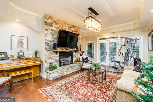 living room featuring hardwood / wood-style flooring, a stone fireplace, ornamental molding, and french doors