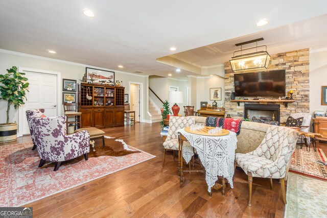 living room featuring a stone fireplace, crown molding, and hardwood / wood-style floors