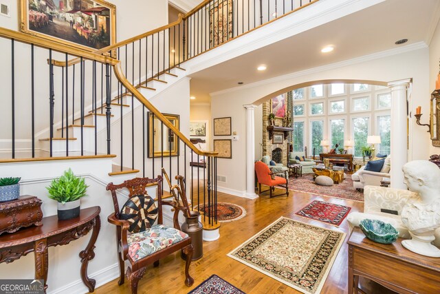 interior space with hardwood / wood-style floors, ornamental molding, a high ceiling, and decorative columns