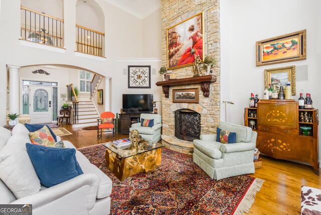 living room featuring a towering ceiling, ornate columns, crown molding, light hardwood / wood-style flooring, and a fireplace