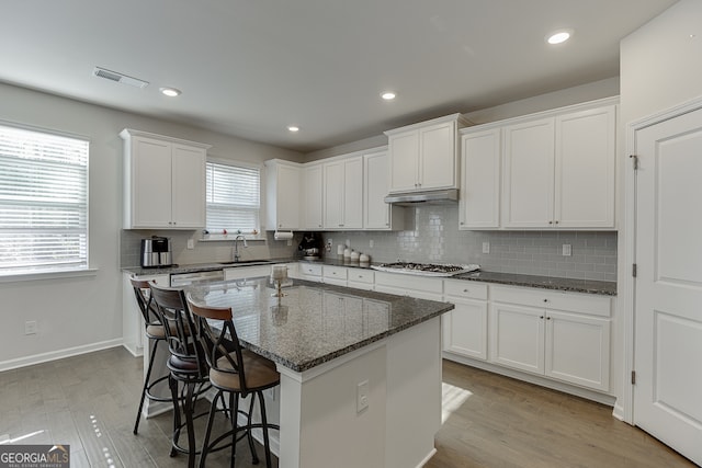 kitchen with a kitchen island, dark stone countertops, plenty of natural light, and white cabinetry