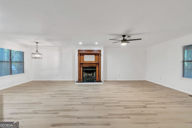 unfurnished living room with ceiling fan with notable chandelier, light hardwood / wood-style floors, and a wealth of natural light