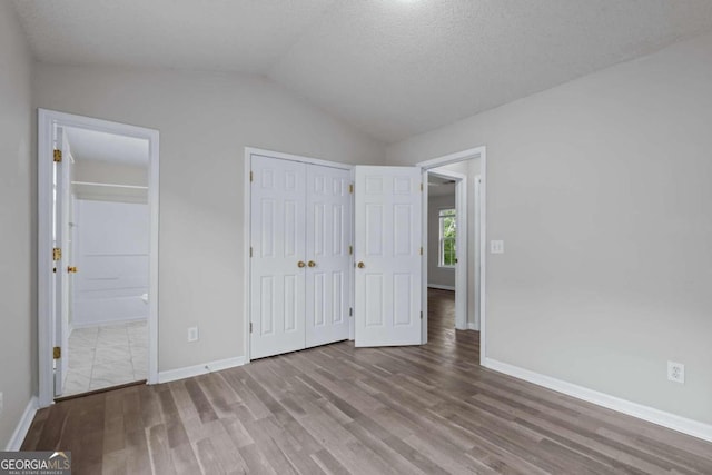 unfurnished bedroom featuring lofted ceiling, connected bathroom, light hardwood / wood-style flooring, and a textured ceiling