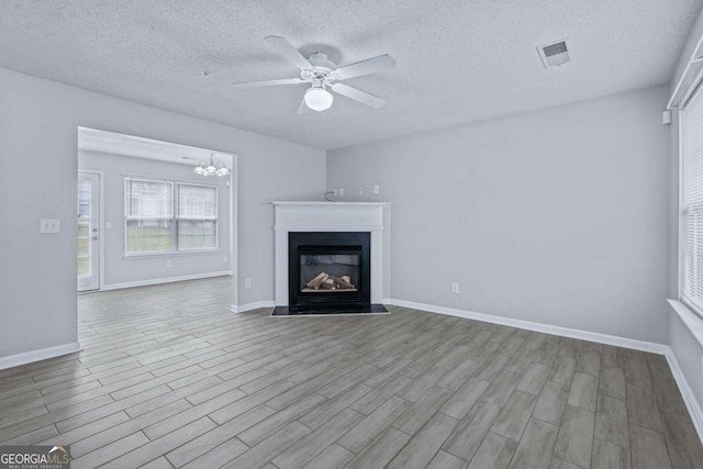 unfurnished living room with ceiling fan with notable chandelier, a textured ceiling, and light wood-type flooring