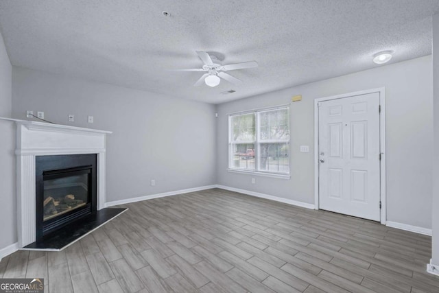 unfurnished living room with ceiling fan, a textured ceiling, and light hardwood / wood-style flooring