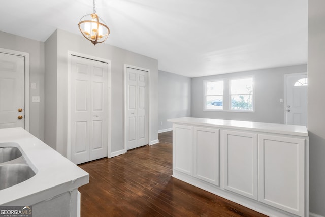 kitchen featuring pendant lighting, white cabinets, sink, a notable chandelier, and dark hardwood / wood-style flooring