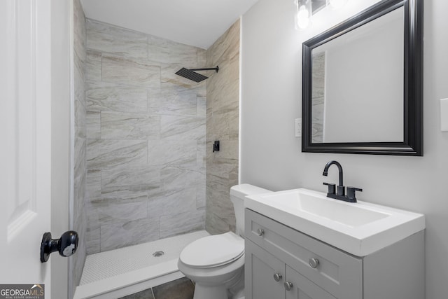 bathroom featuring tile patterned flooring, toilet, tiled shower, and vanity