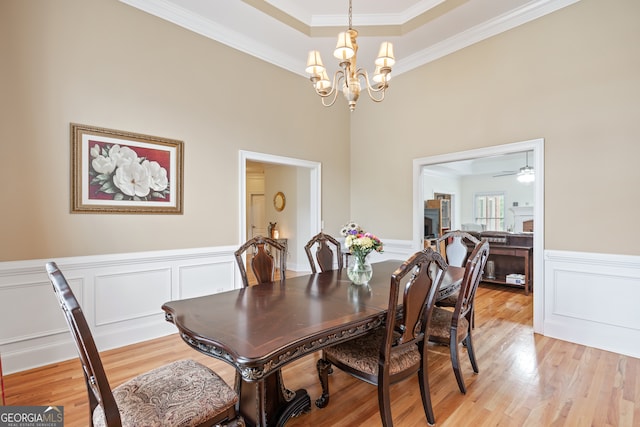 dining space with ceiling fan with notable chandelier, light hardwood / wood-style flooring, ornamental molding, and a high ceiling