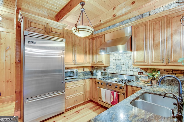 kitchen featuring dark stone counters, wall chimney range hood, sink, and high quality appliances