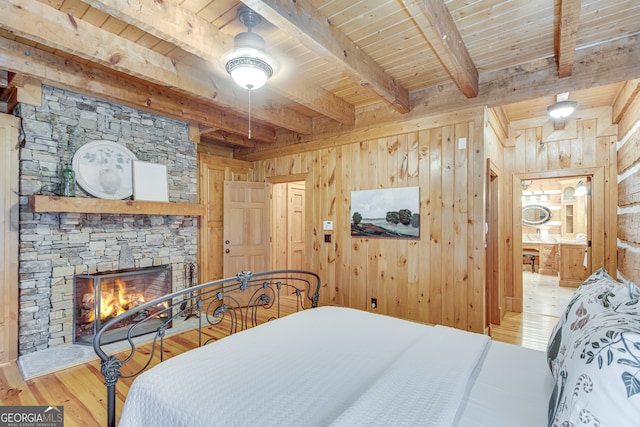 bedroom with wooden walls, a stone fireplace, wood ceiling, light hardwood / wood-style flooring, and beam ceiling