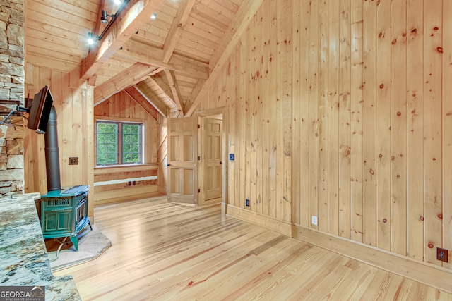 additional living space featuring hardwood / wood-style floors, lofted ceiling with beams, wooden walls, and a wood stove