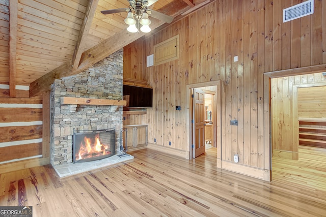 unfurnished living room featuring light wood-type flooring, wooden walls, wooden ceiling, a fireplace, and beam ceiling