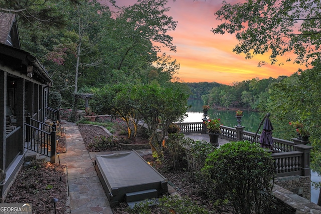 yard at dusk featuring a water view, a sunroom, and a patio area