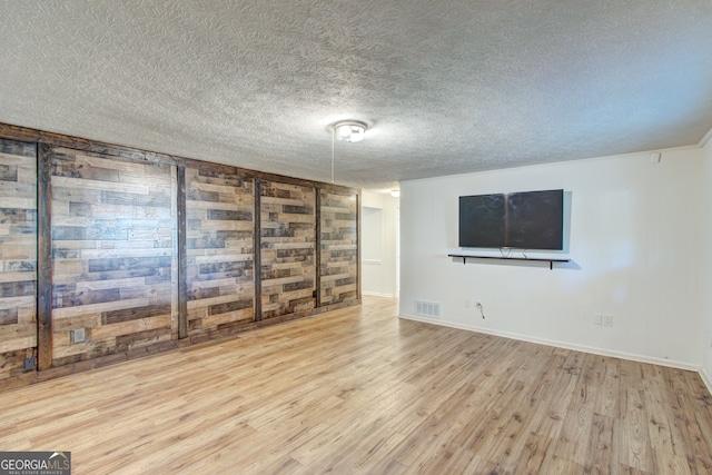 unfurnished room featuring light hardwood / wood-style flooring, wooden walls, and a textured ceiling