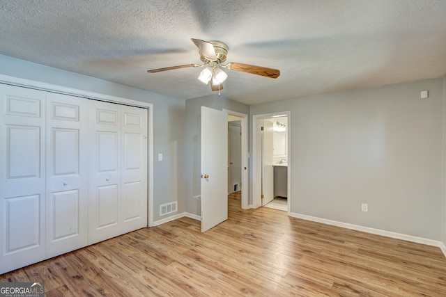 unfurnished bedroom with ceiling fan, a closet, light hardwood / wood-style floors, ensuite bath, and a textured ceiling