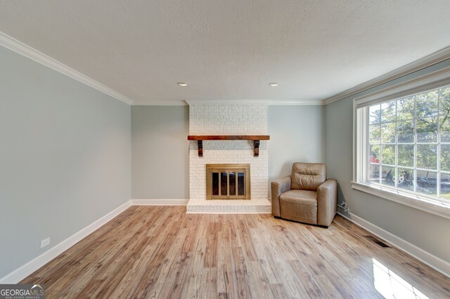 unfurnished room with a brick fireplace, ornamental molding, light hardwood / wood-style flooring, and a textured ceiling