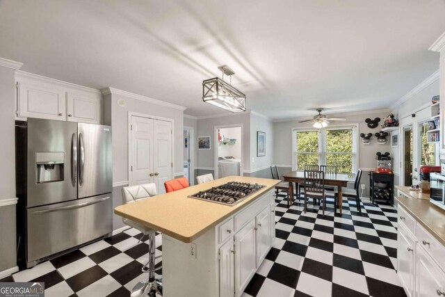 kitchen featuring a kitchen island, stainless steel appliances, white cabinetry, washer and dryer, and a kitchen breakfast bar