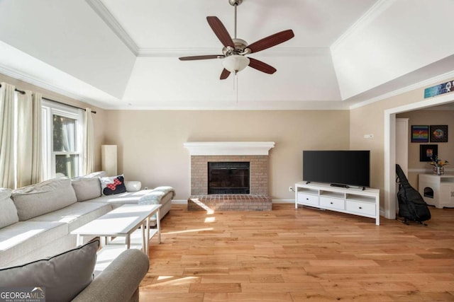 living room featuring ceiling fan, light hardwood / wood-style flooring, a raised ceiling, a fireplace, and ornamental molding