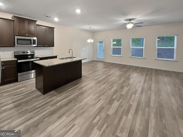 kitchen with appliances with stainless steel finishes, a healthy amount of sunlight, light hardwood / wood-style flooring, and an island with sink