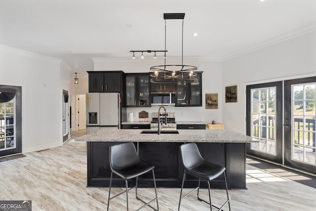 kitchen featuring appliances with stainless steel finishes, french doors, a center island with sink, and light hardwood / wood-style floors