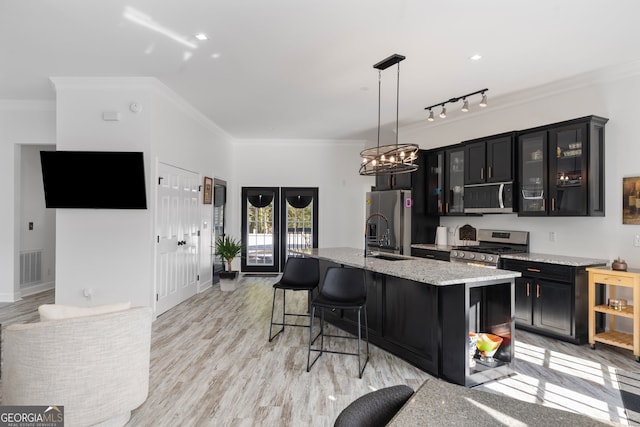 kitchen featuring an island with sink, stainless steel appliances, crown molding, sink, and decorative light fixtures