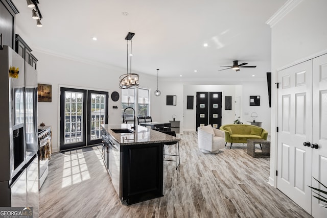 kitchen with light stone counters, a breakfast bar area, a kitchen island with sink, crown molding, and sink