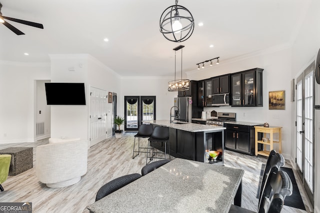 kitchen with an island with sink, stainless steel appliances, decorative light fixtures, light stone counters, and a breakfast bar area