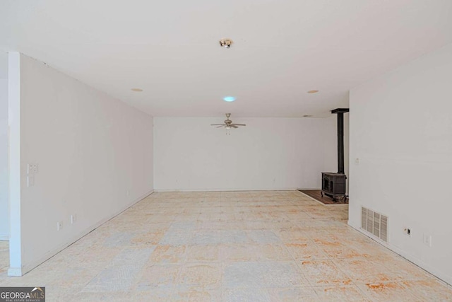 unfurnished living room with a wood stove and ceiling fan