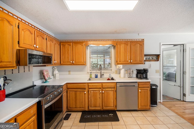 kitchen with a textured ceiling, appliances with stainless steel finishes, sink, and light hardwood / wood-style flooring