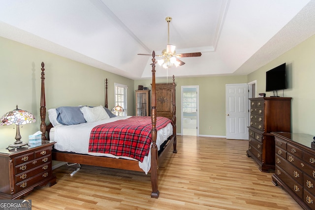 bedroom with connected bathroom, a tray ceiling, ceiling fan, and light hardwood / wood-style flooring