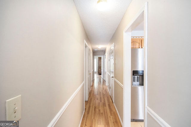 corridor with a textured ceiling and light hardwood / wood-style floors