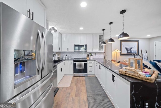 kitchen with white cabinets, decorative light fixtures, backsplash, light hardwood / wood-style flooring, and appliances with stainless steel finishes