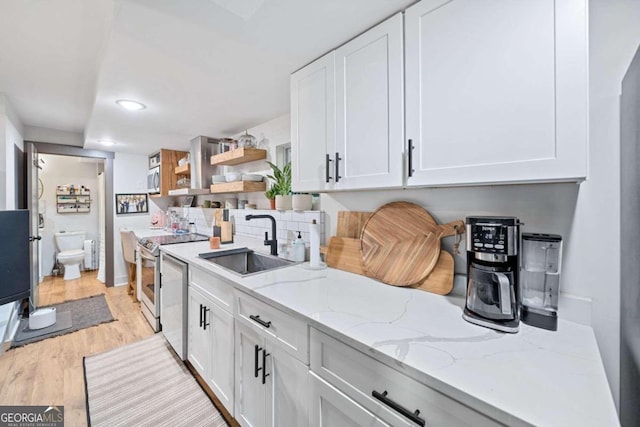 kitchen featuring light wood-type flooring, light stone countertops, stainless steel appliances, sink, and white cabinetry